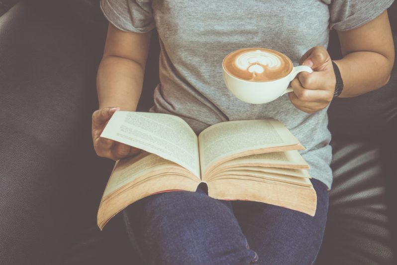 Woman reading a book holding a cup of coffee