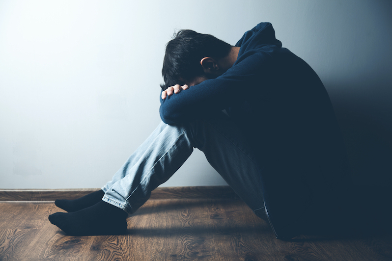A teenage boy sitting on the floor in a dark room looking sad