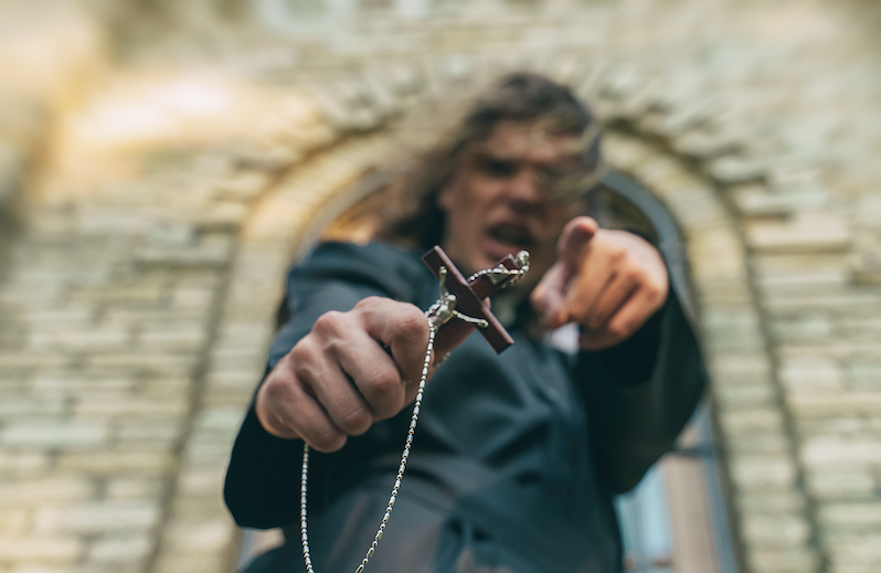 An angry man standing outside a church holding a cross, he is pointing and shouting