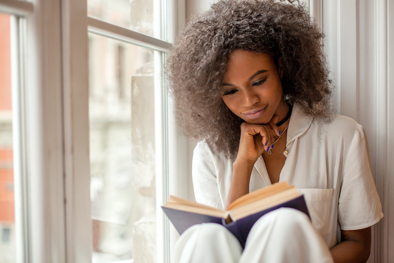 A young woman sitting by a window reading a book