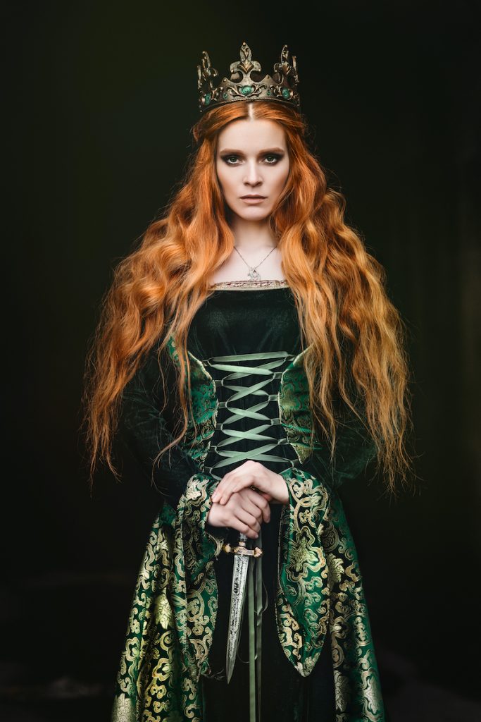 A lady with long red hair wearing a medieval style dress and a crown