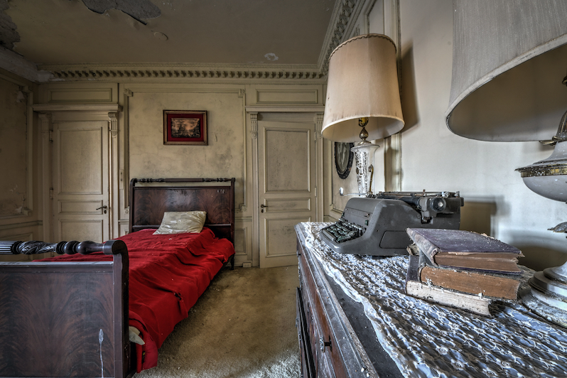 A bedroom in an abandoned house. A bed and a lamp are visible.