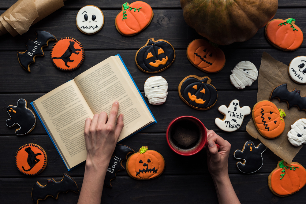 Top view of a woman reading a book surrounded by Halloween cookies